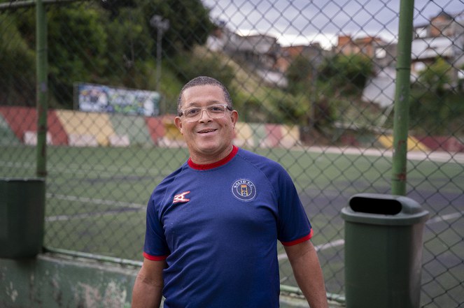 Caravana das Periferias vai a territórios afetados por desastres em São Paulo Homem sorrindo para o fotógrafo em frente a quadra poliesportiva.