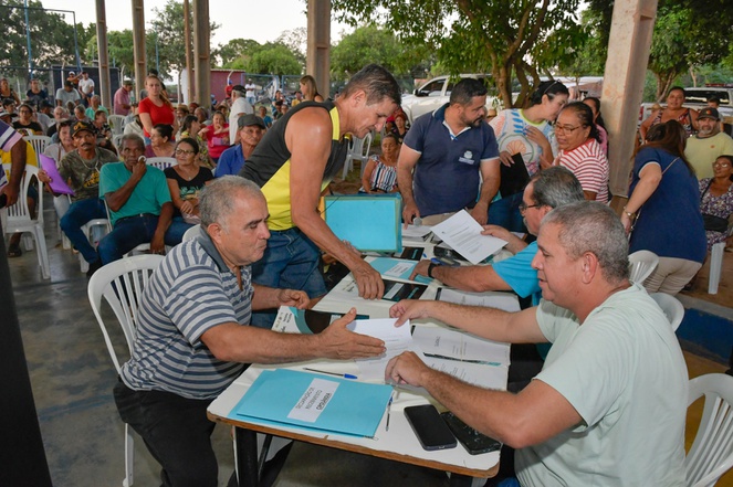 Na imagem pessoas reunidas assinando documento de posse de casas.